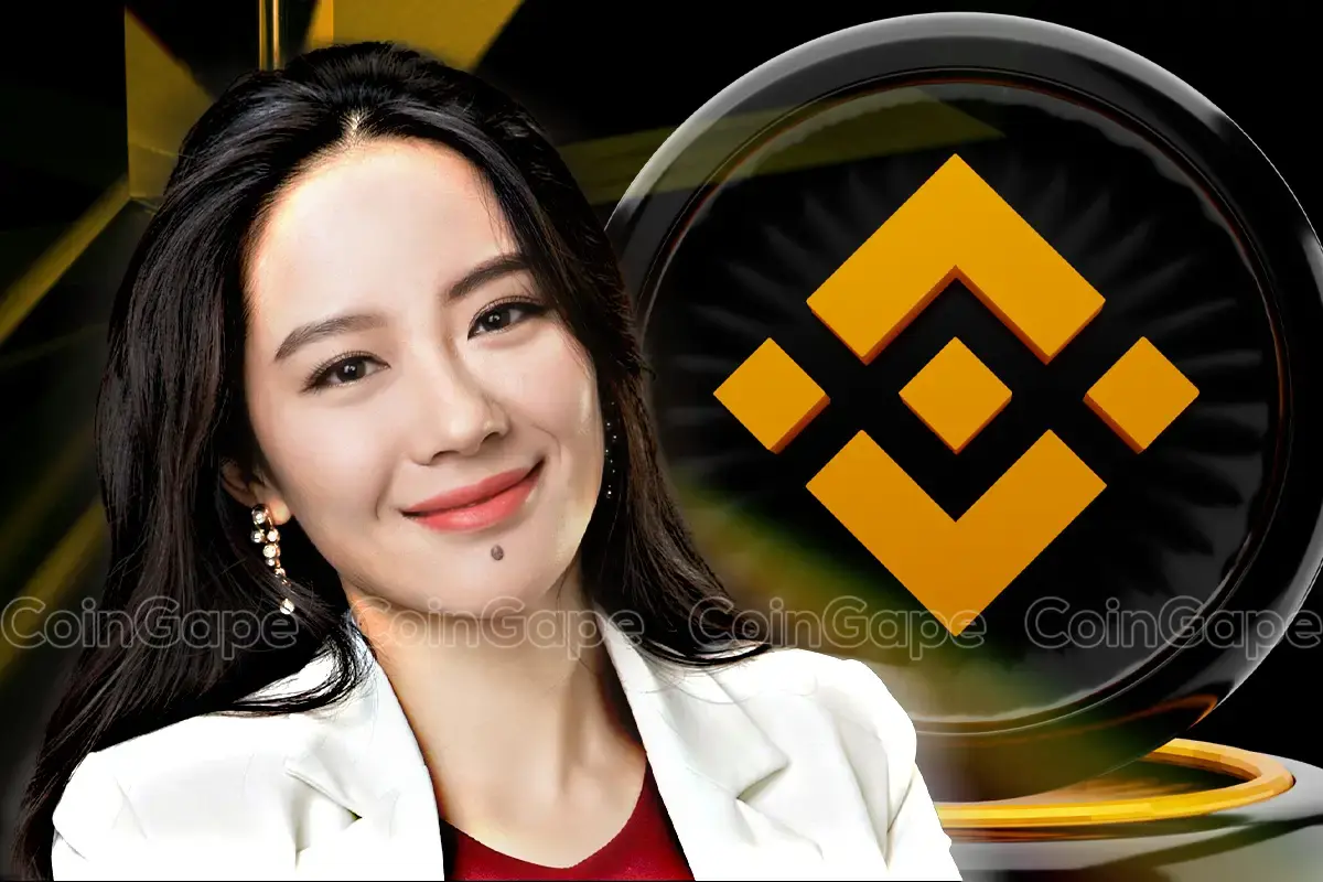 Retrato de uma mulher asiática sorrindo, vestindo blazer branco e blusa vermelha, com o logotipo dourado da Binance ao fundo.