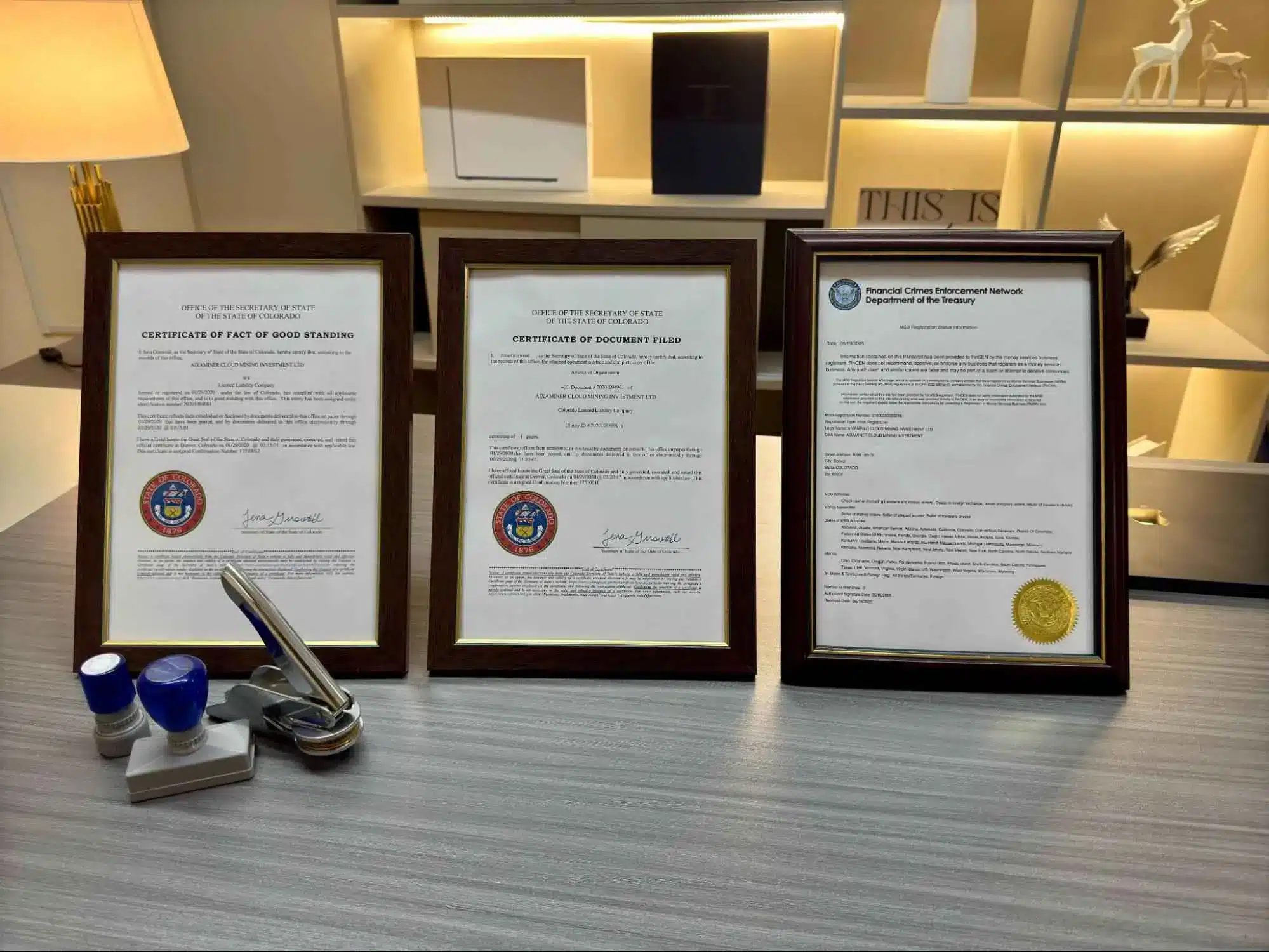 Três certificados oficiais emoldurados exibindo Certificate of Good Standing do Colorado, Certificate of Document Filed e documento do Financial Crimes Enforcement Network do Departamento do Tesouro americano.