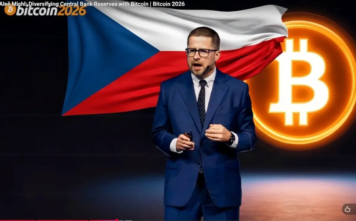 Aleš Michl, governador do Banco Nacional Tcheco, discursa na Bitcoin 2026 com a bandeira da República Tcheca e o símbolo do Bitcoin ao fundo.