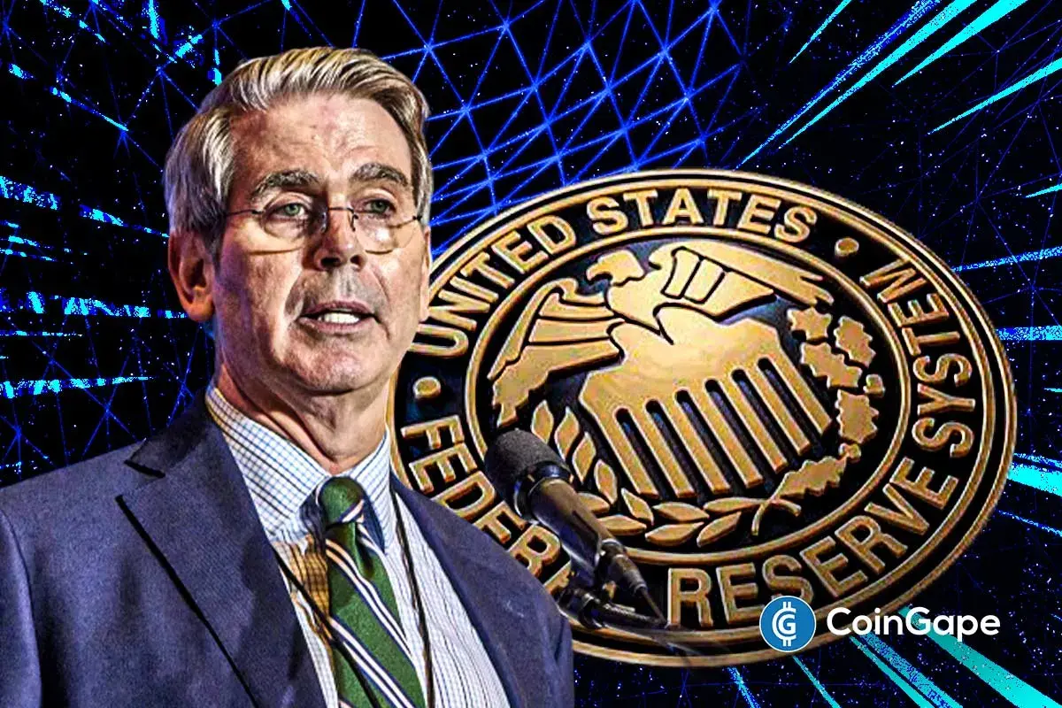 Homem com cabelos grisalhos em frente ao selo dourado do Federal Reserve System dos Estados Unidos.
