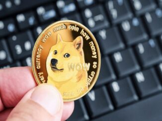 Mão segura uma moeda dourada de Dogecoin com o cão Shiba Inu e a inscrição "wow" sobre um teclado preto.