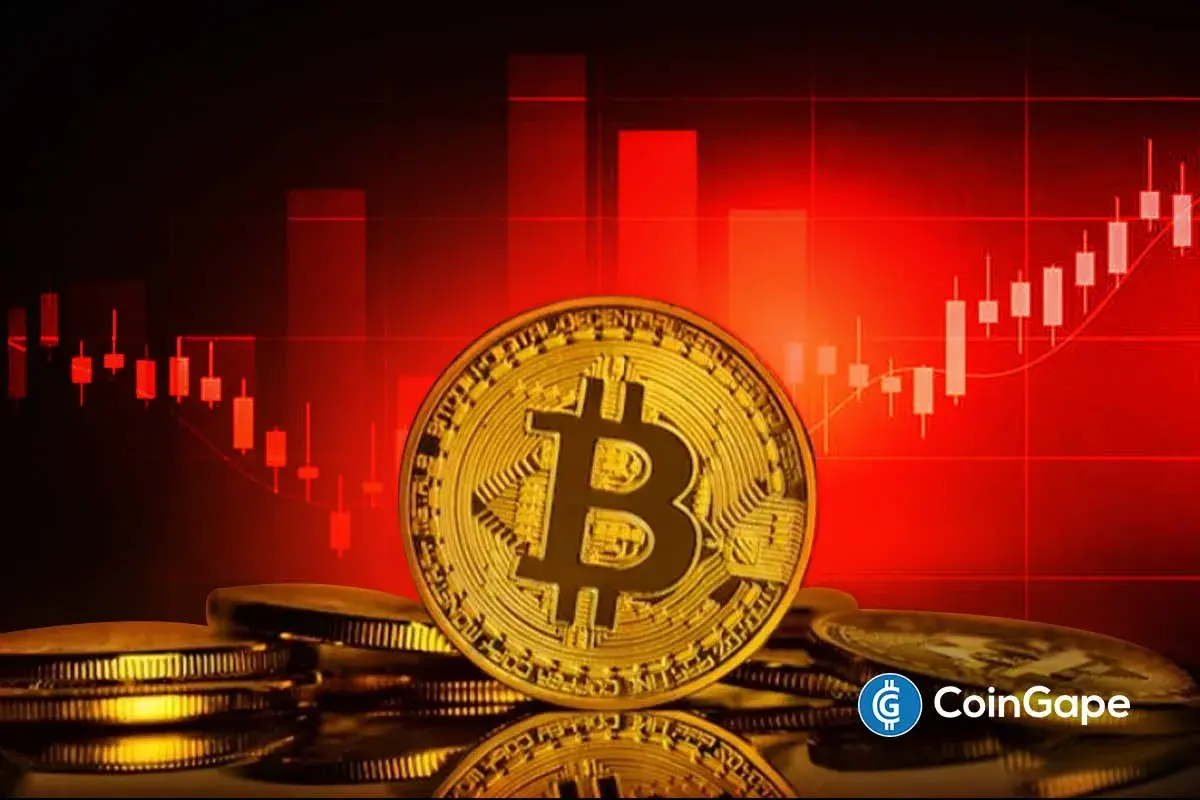Moeda física de Bitcoin dourada sobre pilha de moedas, com gráfico de candles vermelho ao fundo e logo da CoinGape.